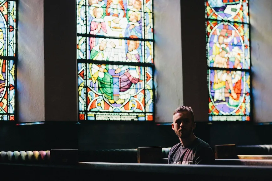 Person sitting in a church pew under stained-glass windows