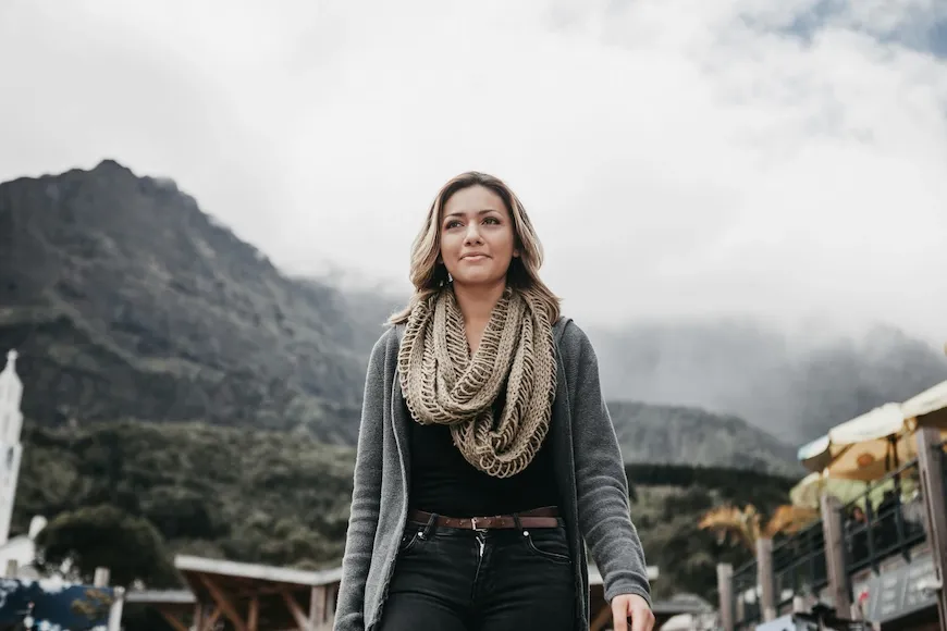 Woman in a scarf standing outdoors in front of mountains