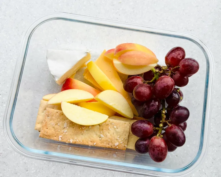 Homemade cheese and fruit protein box with apple slices and red grapes
