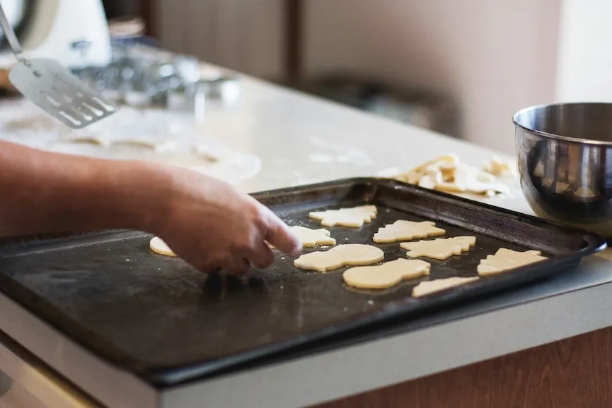 Hands placing cut-out sugar cookies on a baking sheet