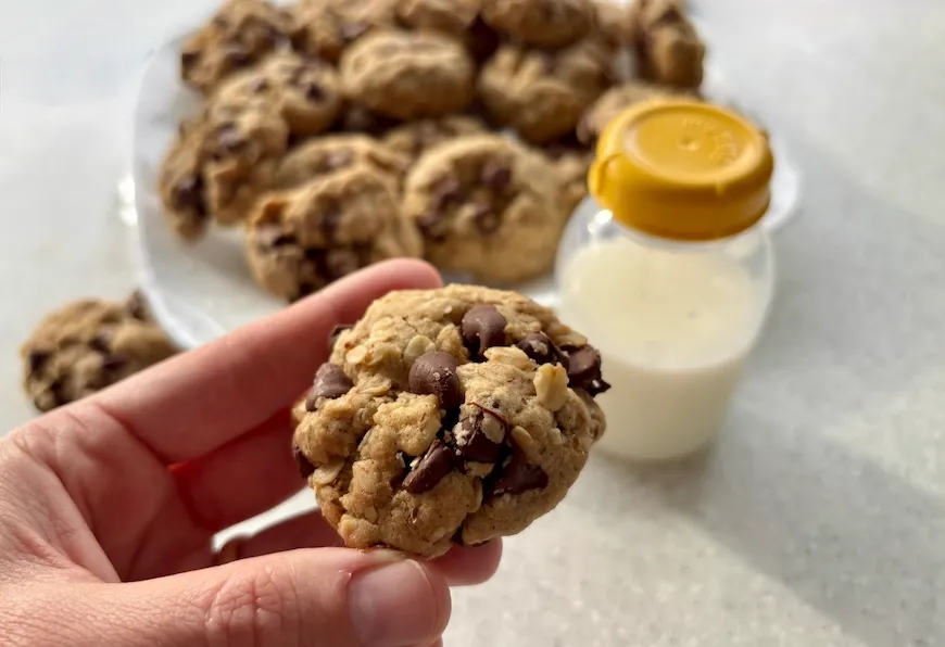 Hand holding a chocolate chip lactation cookie next to a glass of milk