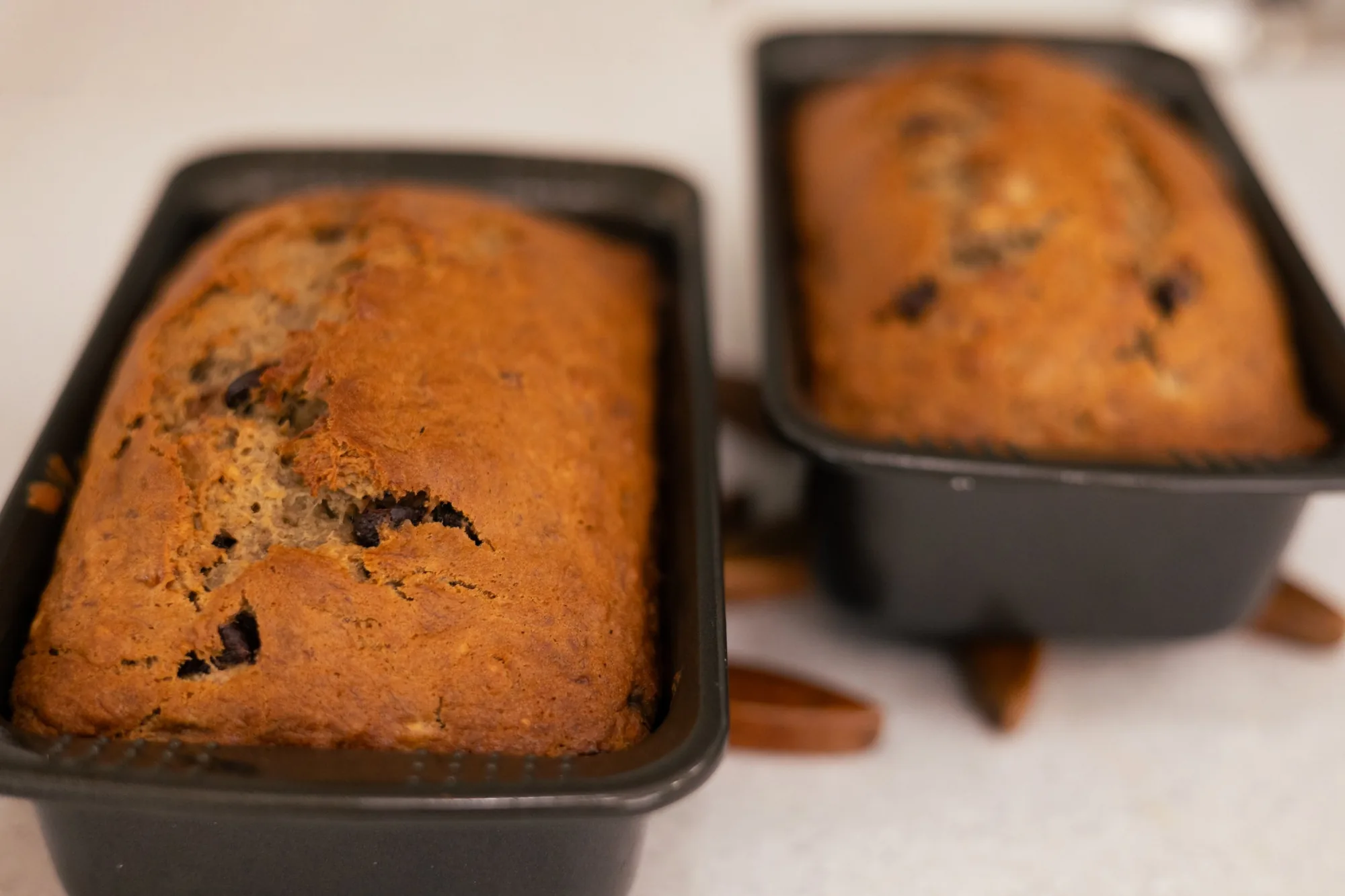 Two loaves of chocolate chip banana bread cooling in dark metal loaf pans