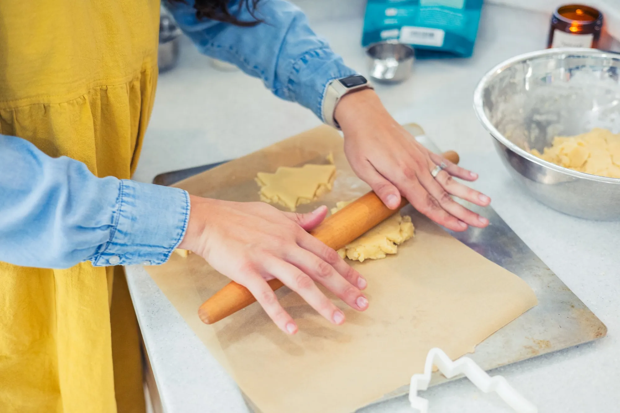 Hands rolling out sugar cookie dough on parchment beside a Christmas tree cookie cutter