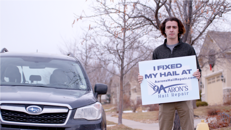 Young driver with his Subaru holding an I fixed my hail at Aaron's sign