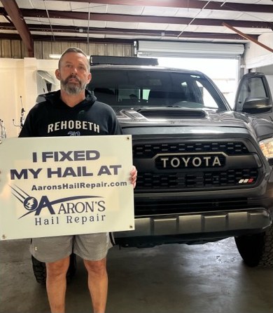 Customer with his Toyota Tacoma holding an I fixed my hail at Aaron's sign