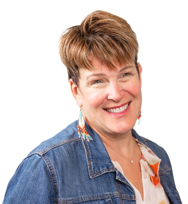 Pam Grahame, Execution & Transformation — Smiling person with short hair wearing a denim jacket and beaded earrings, against a white background
