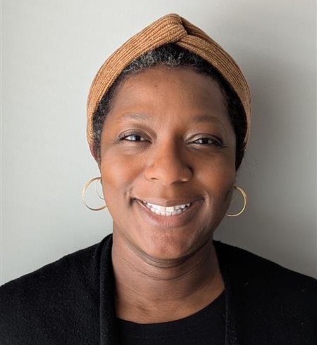 Abiola Agbayewa, Engagement & Communications — Smiling person wearing a tan headband, gold hoop earrings, and a black cardigan, against a light background