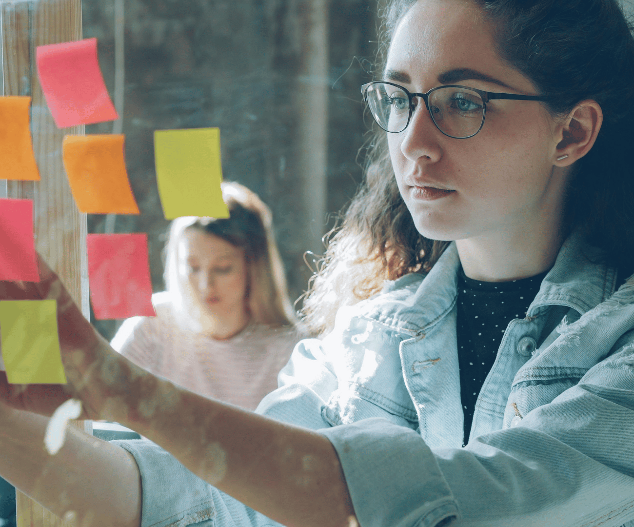 Eine Frau und ein Mann stehen vor einer Glasscheibe, auf der bunte Klebezettel kleben.