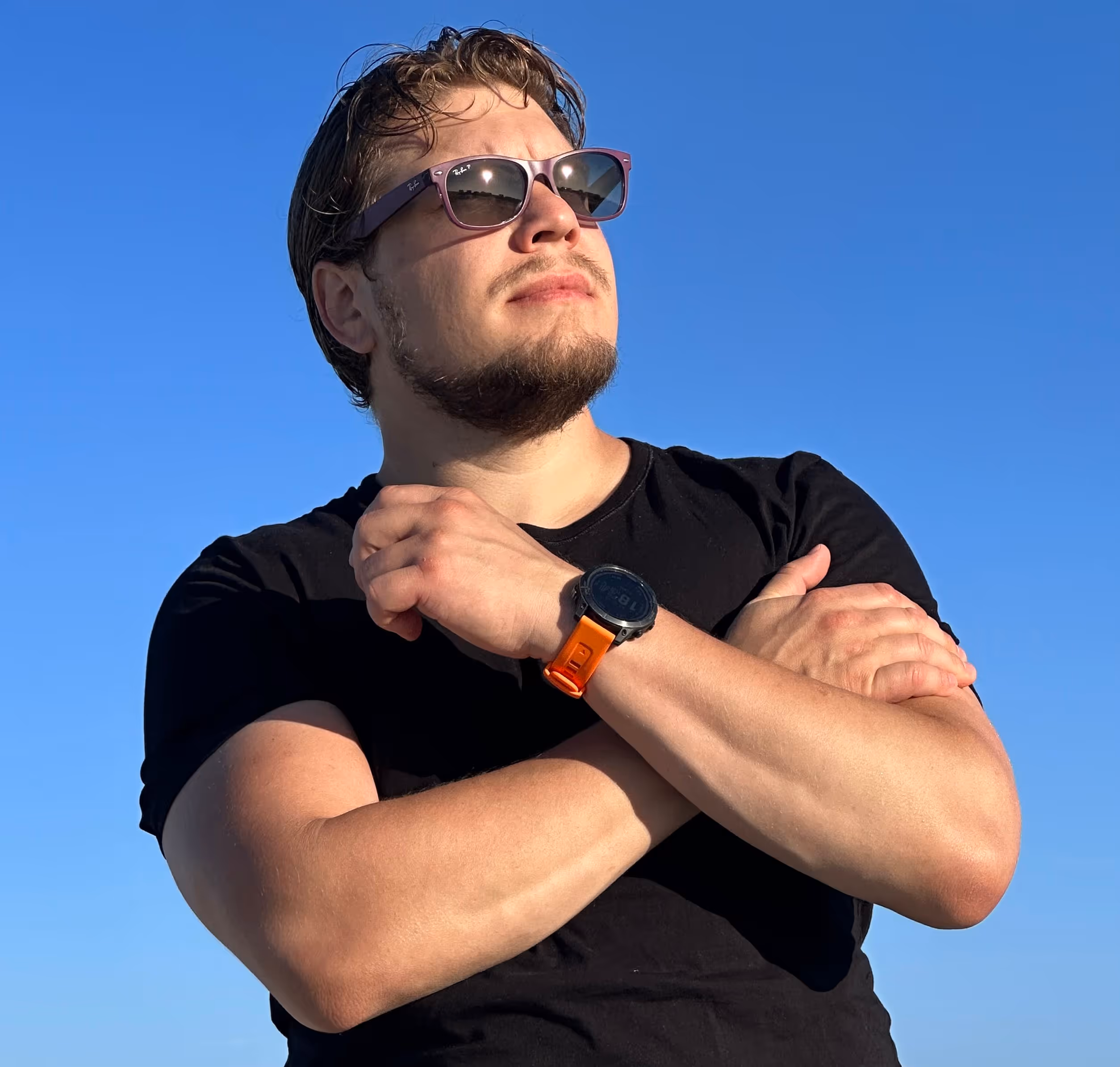 Anton is wearing a black t-shirt, purple sunglasses is confidently looking at the horizon. The sky is in the background and the sun is shining at him.