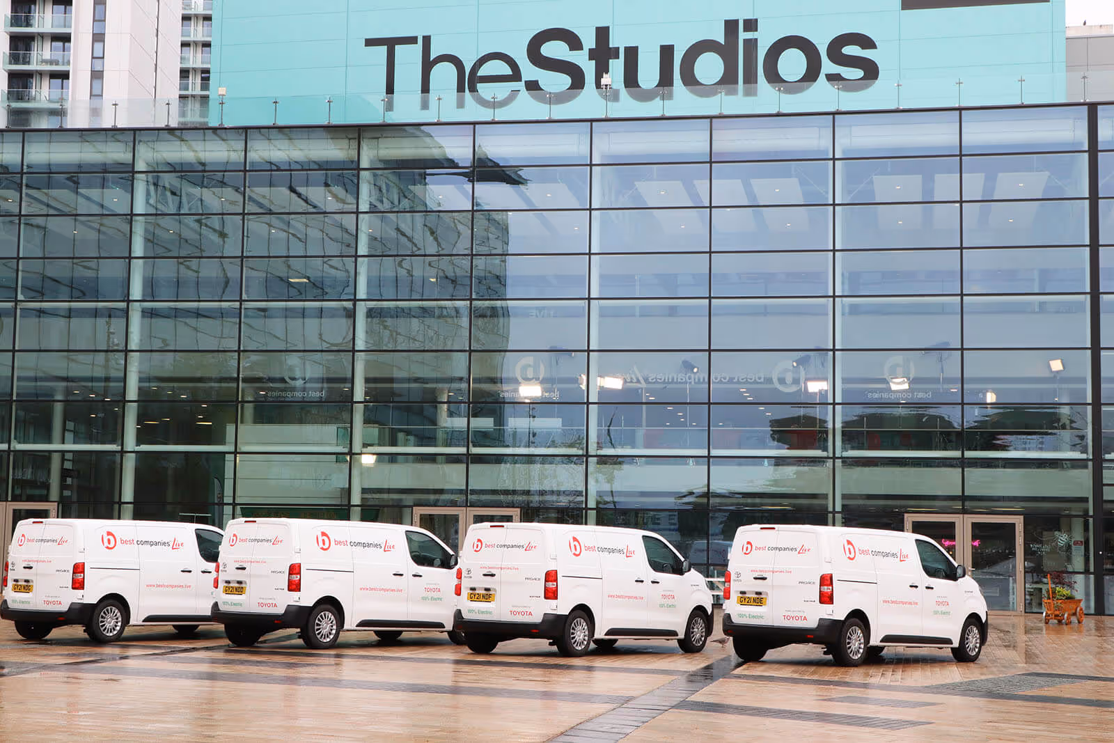 Four electric vans with Best Companies Live branding parked outside of the studio at Media City
