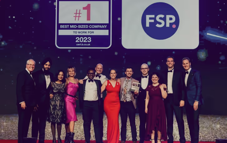A group of formally dressed people standing on a stage under signs reading '#1 Best Mid-Sized Company to Work For 2023' and 'FSP'.