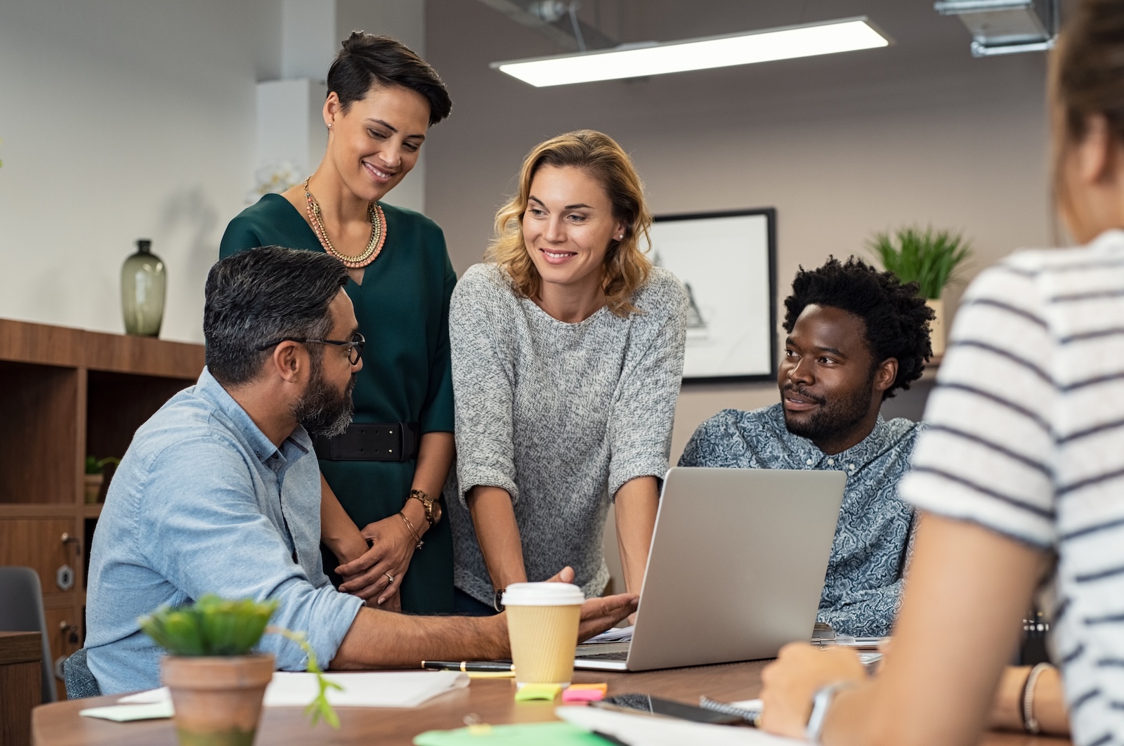 Diverse team of four collaborating around a laptop in a modern office setting.