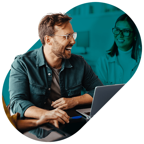 Two people smiling and talking while sitting at a table with a laptop during a meeting.