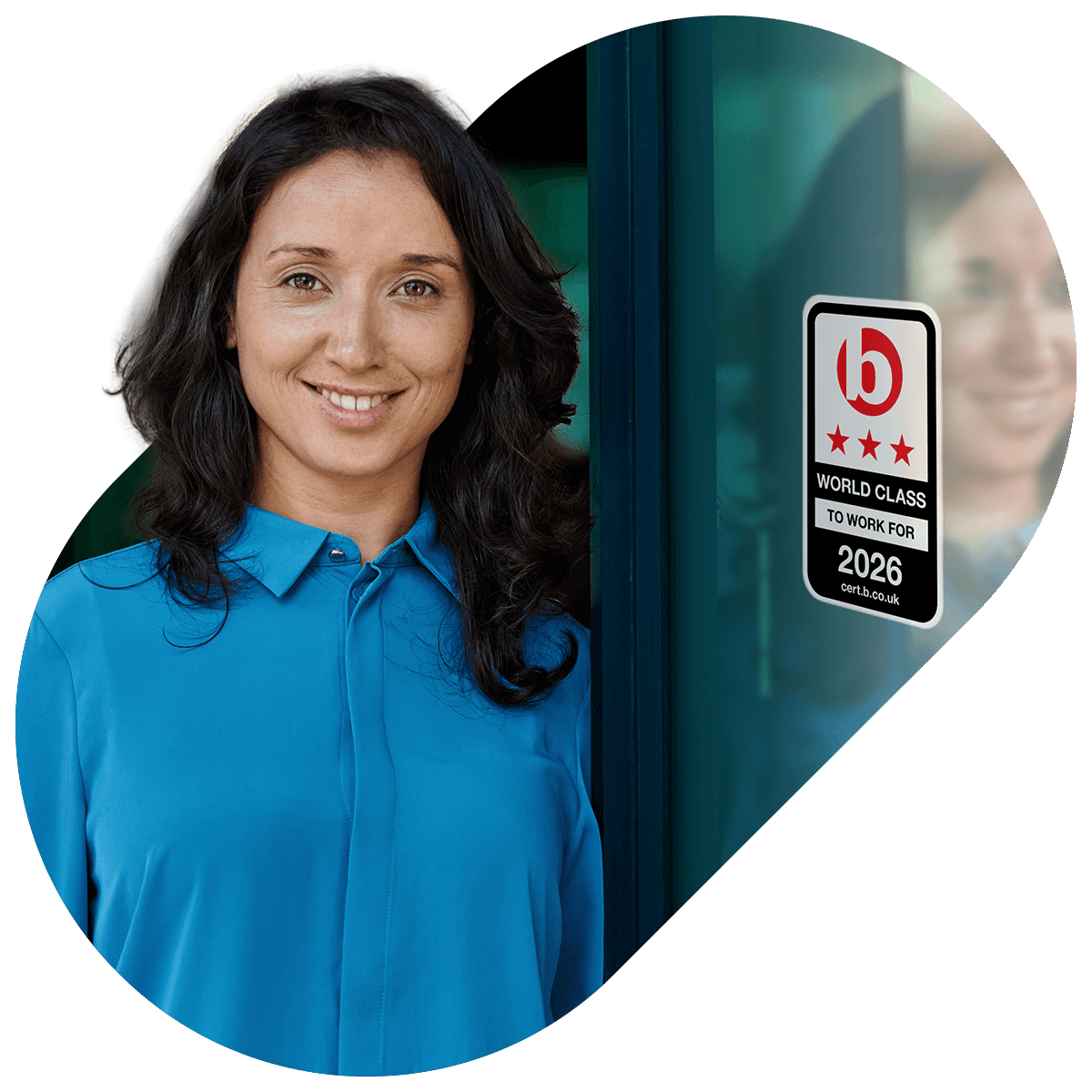 Smiling woman with dark hair wearing a blue blouse standing next to a glass door with a 'World Class to Work For 2026' certification sticker.