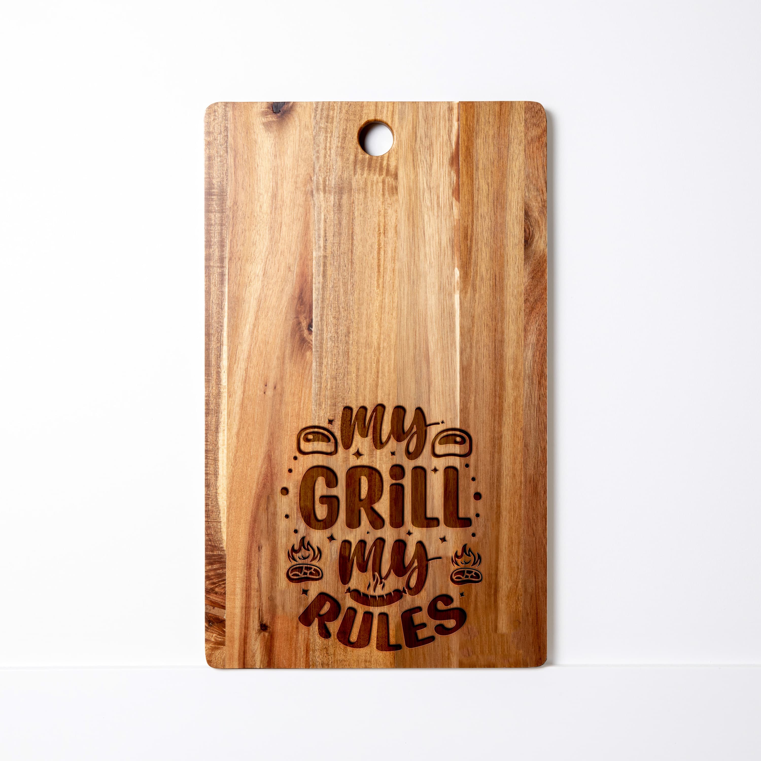 Acacia wood cutting board engraved with the phrase ‘My Grill My Rules’ in bold, playful lettering, featuring grill icons and decorative accents.
