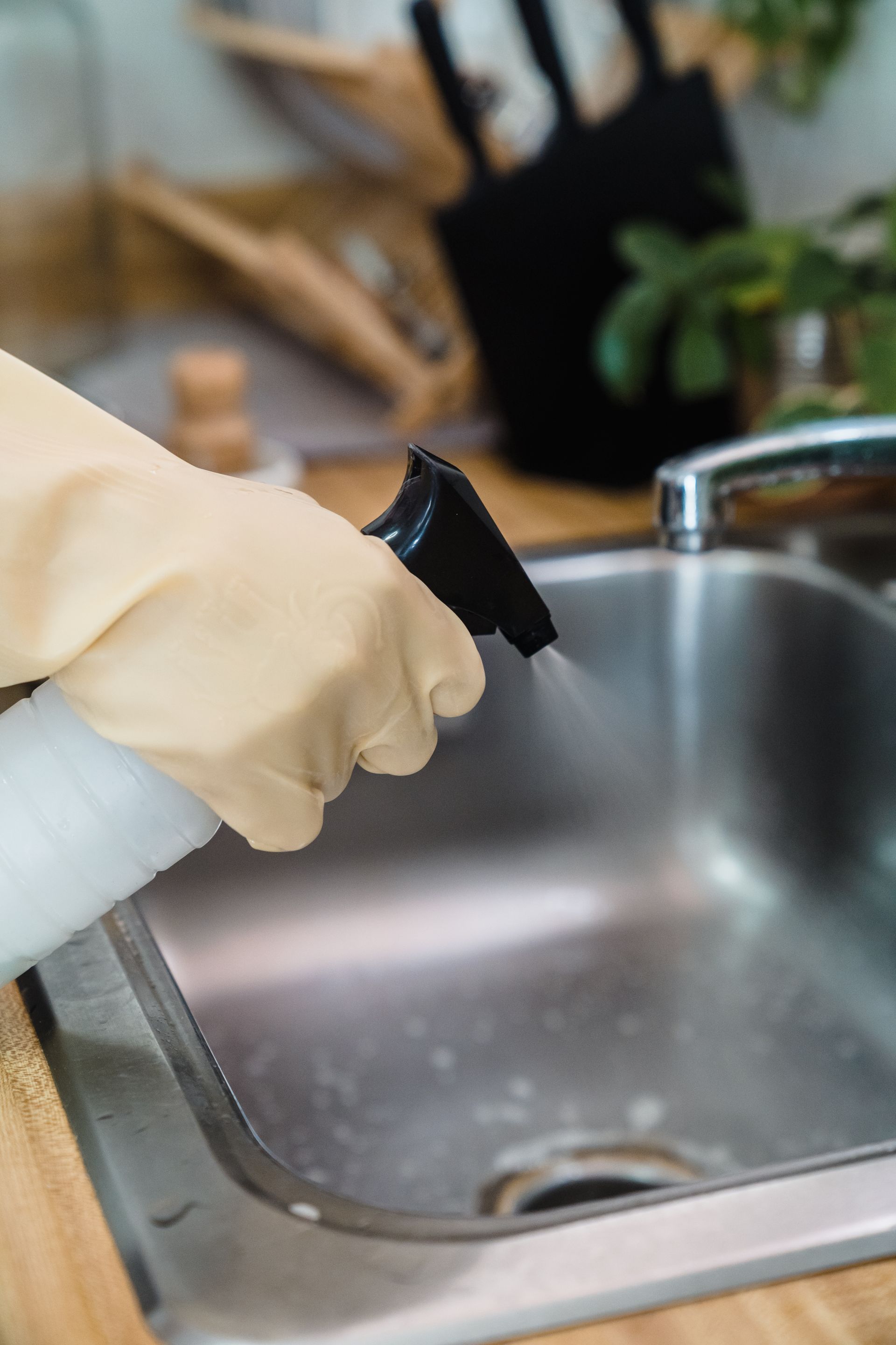 Gloved cleaner spraying and wiping a kitchen sink