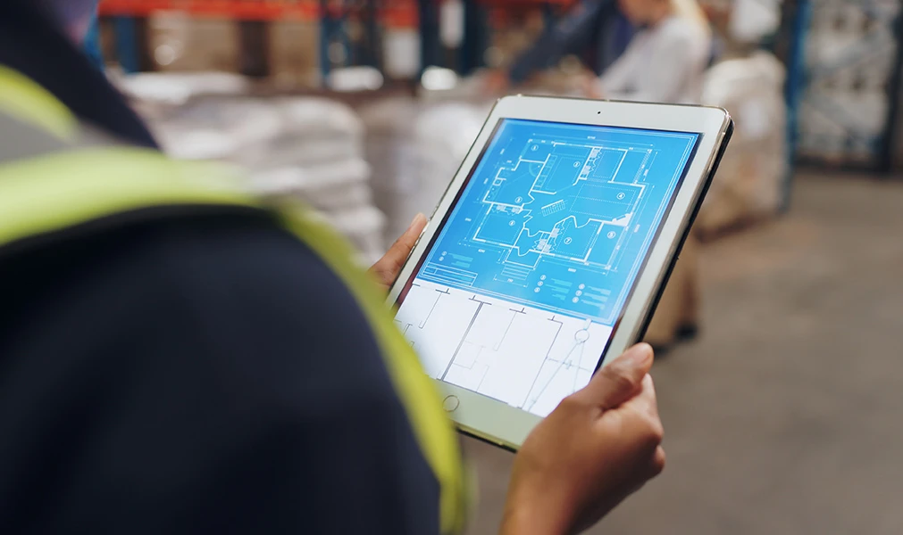 Engineer on tablet or rugged laptop, referencing digital blueprints at a construction site. 