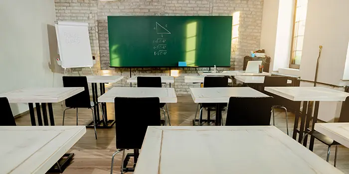 Empty classroom with white desks, black chairs, a green chalkboard displaying a math triangle, and a blank flip chart.