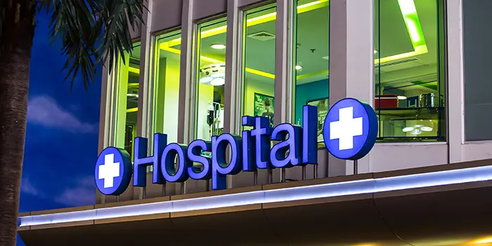 Illuminated blue hospital sign with white medical crosses on a building at night.