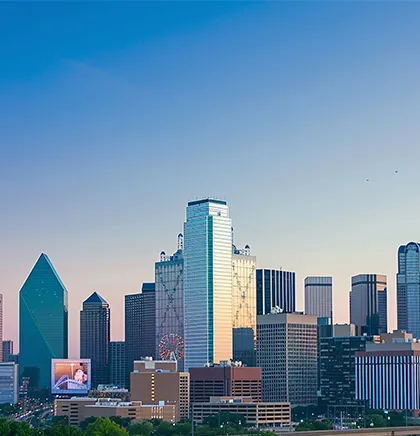 Dallas skyline at sunset with clear sky, showing prominent skyscrapers including the green triangular-shaped building and a Ferris wheel.