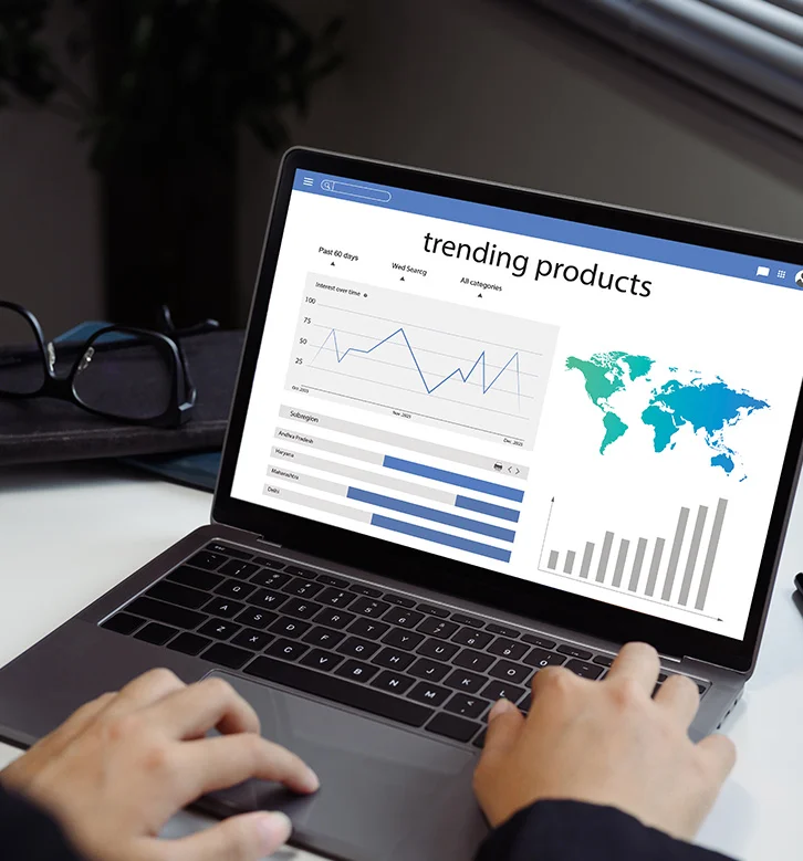 Person using a laptop showing charts and a world map under the heading 'trending products'.