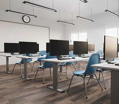 Modern classroom with rows of desks each equipped with computer monitors and blue chairs on wood flooring.
