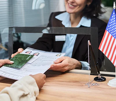 A woman behind a service counter processing a visa application with an American flag visible on the desk.