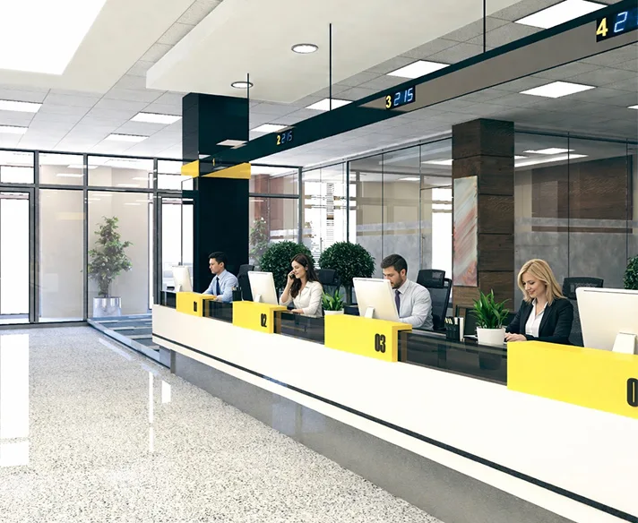 Modern bank interior with four tellers seated behind numbered counters working on computers.