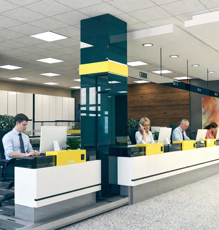 Modern bank counter with four tellers working on computers, one talking on a phone.