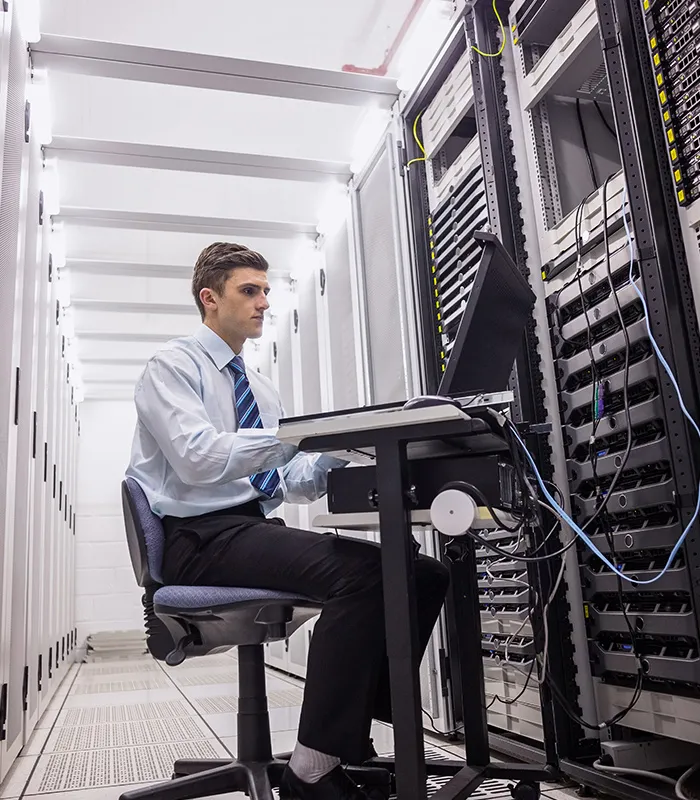 Technician in a dress shirt and tie sitting on a swivel chair using a laptop to diagnose servers in a data center.