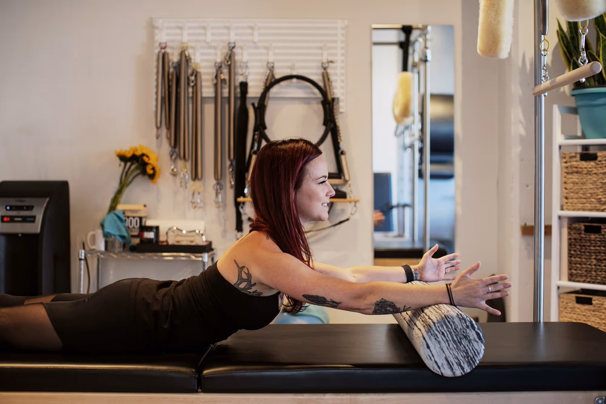 Red headed pilates instructor dressed in black practices spine extension on the foam roller