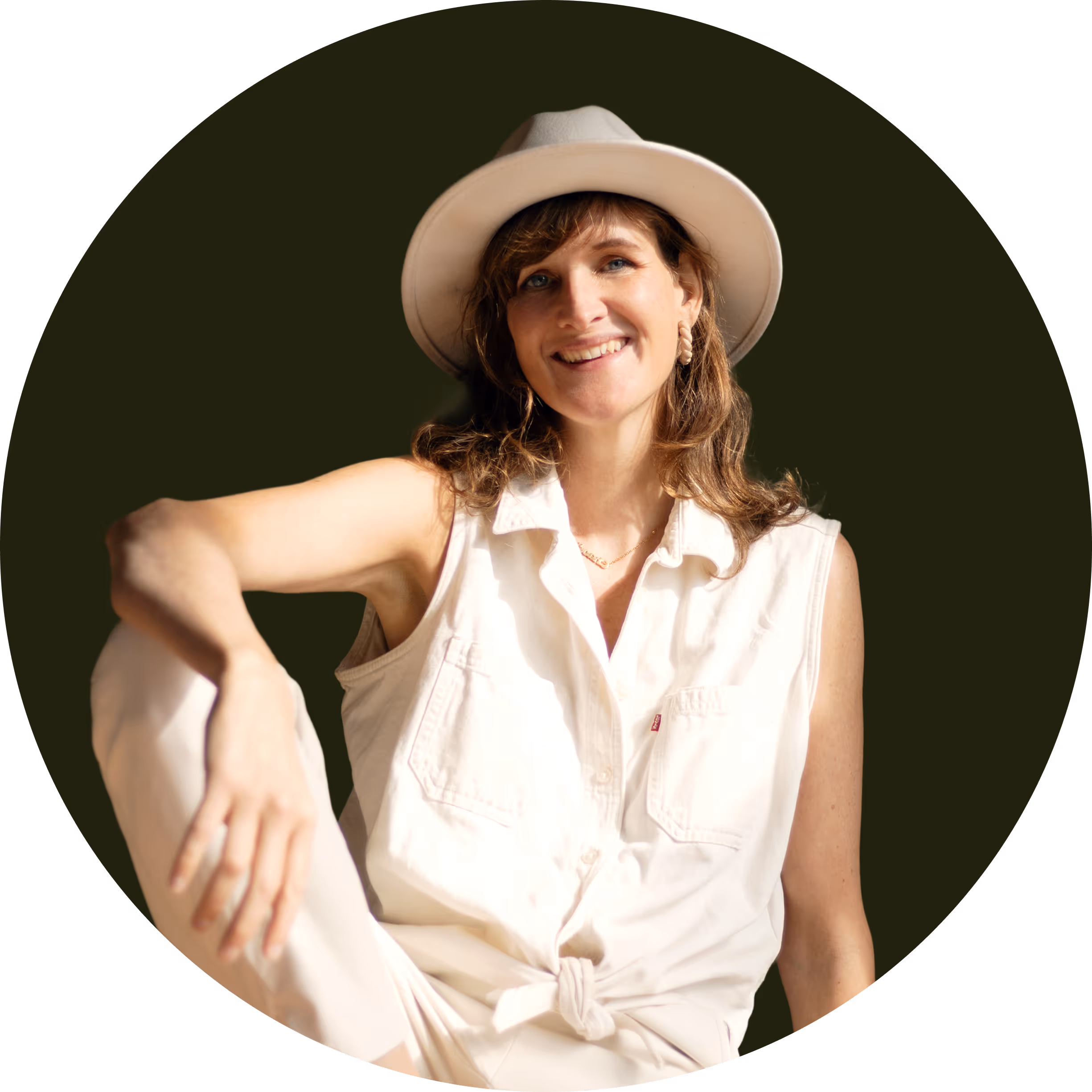 Smiling woman wearing a beige hat and sleeveless white shirt sitting with one arm resting on her knee against a dark circular background.
