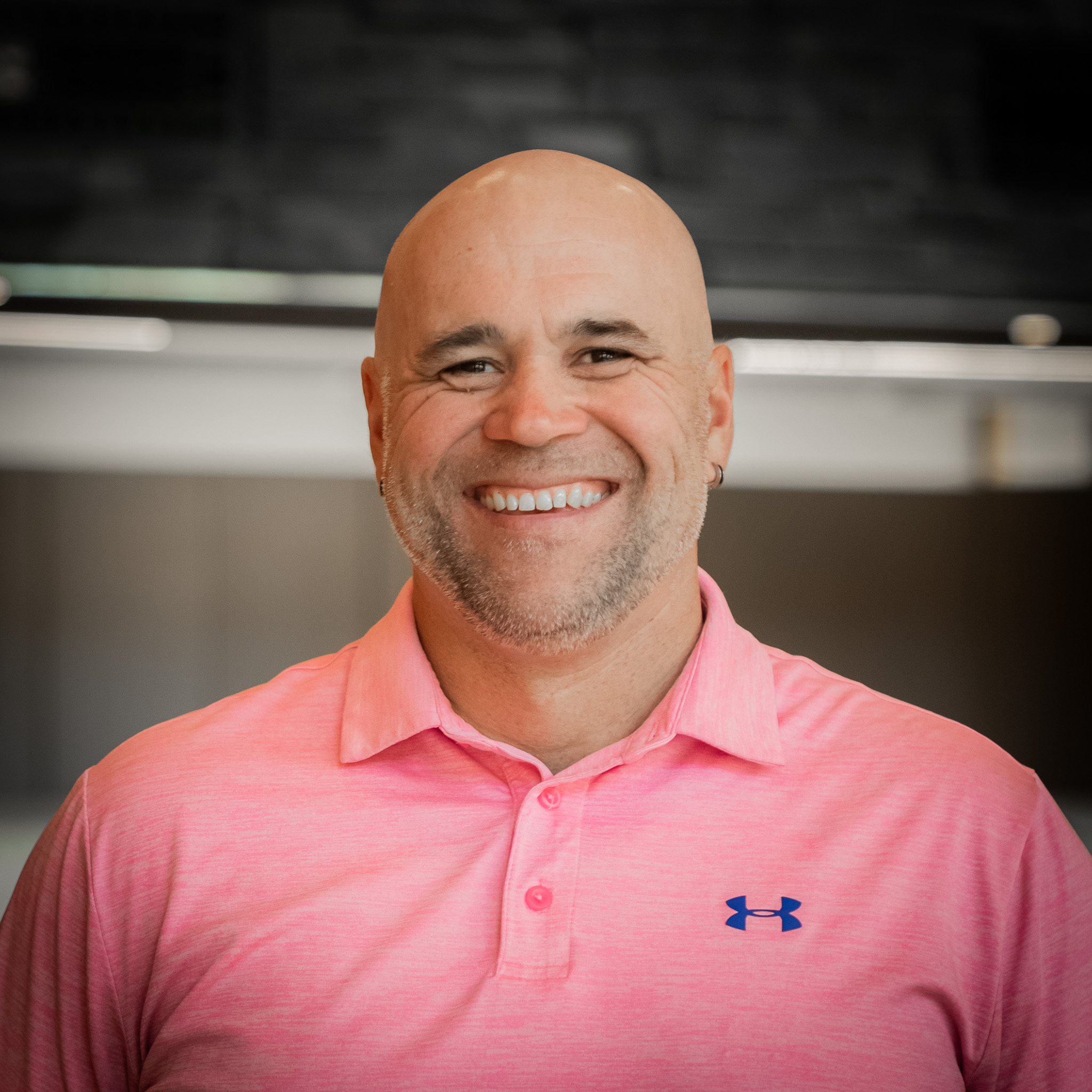 man with short beard smiling and wearing pink shirt