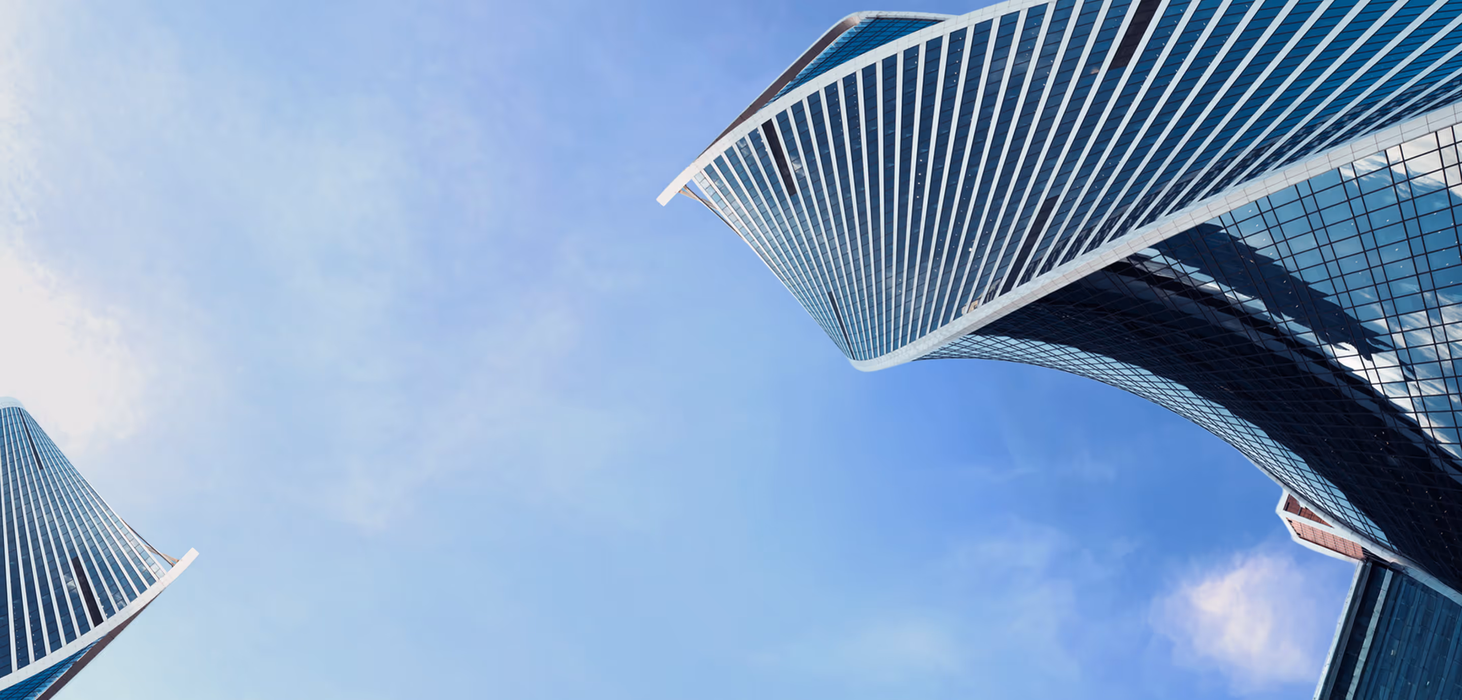 Blick nach oben auf zwei moderne, kurvenförmige Wolkenkratzer mit Glasfassaden vor blauem Himmel.