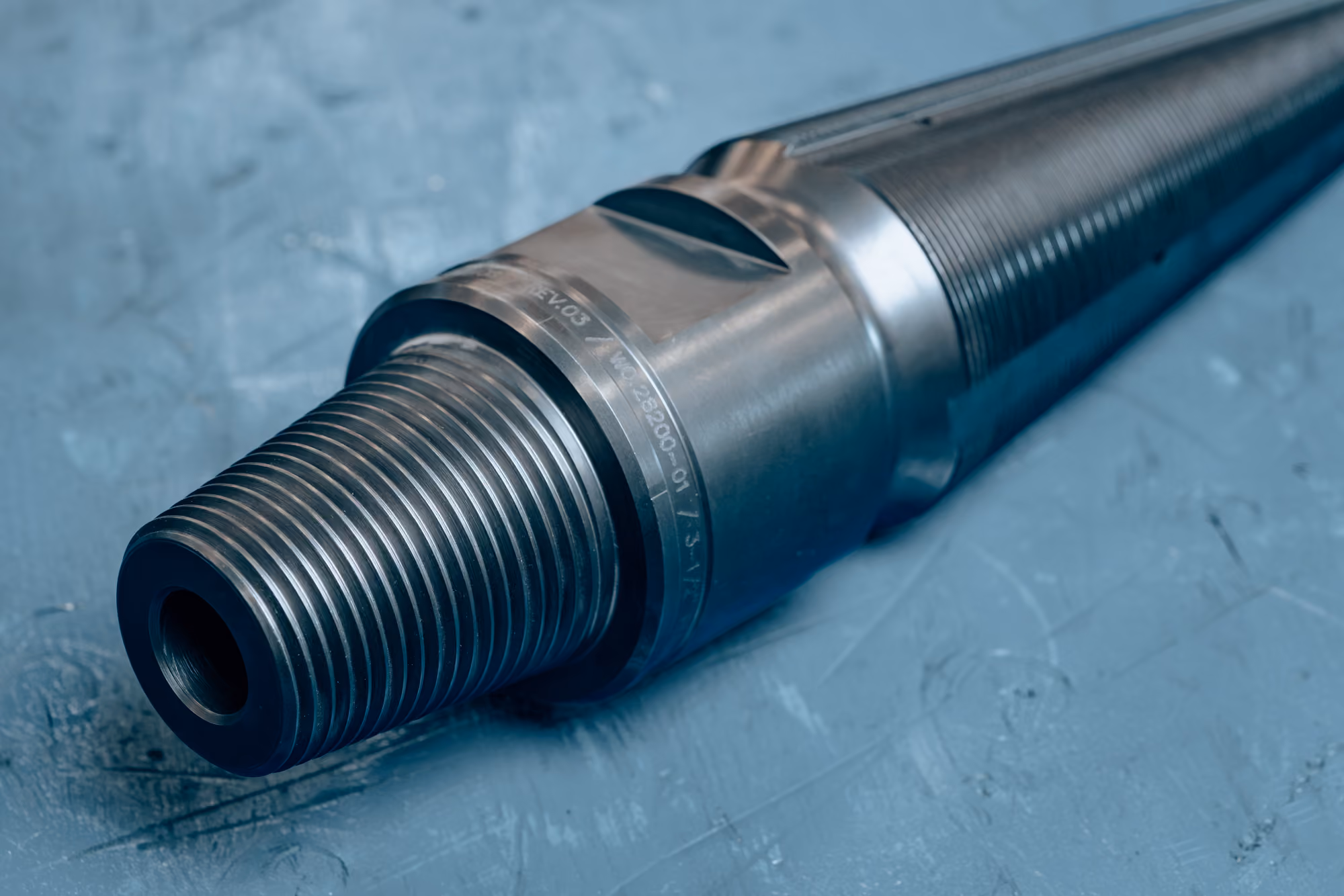 Close-up of a threaded metal cylindrical tool or component with a textured grip section, resting on a blue surface.