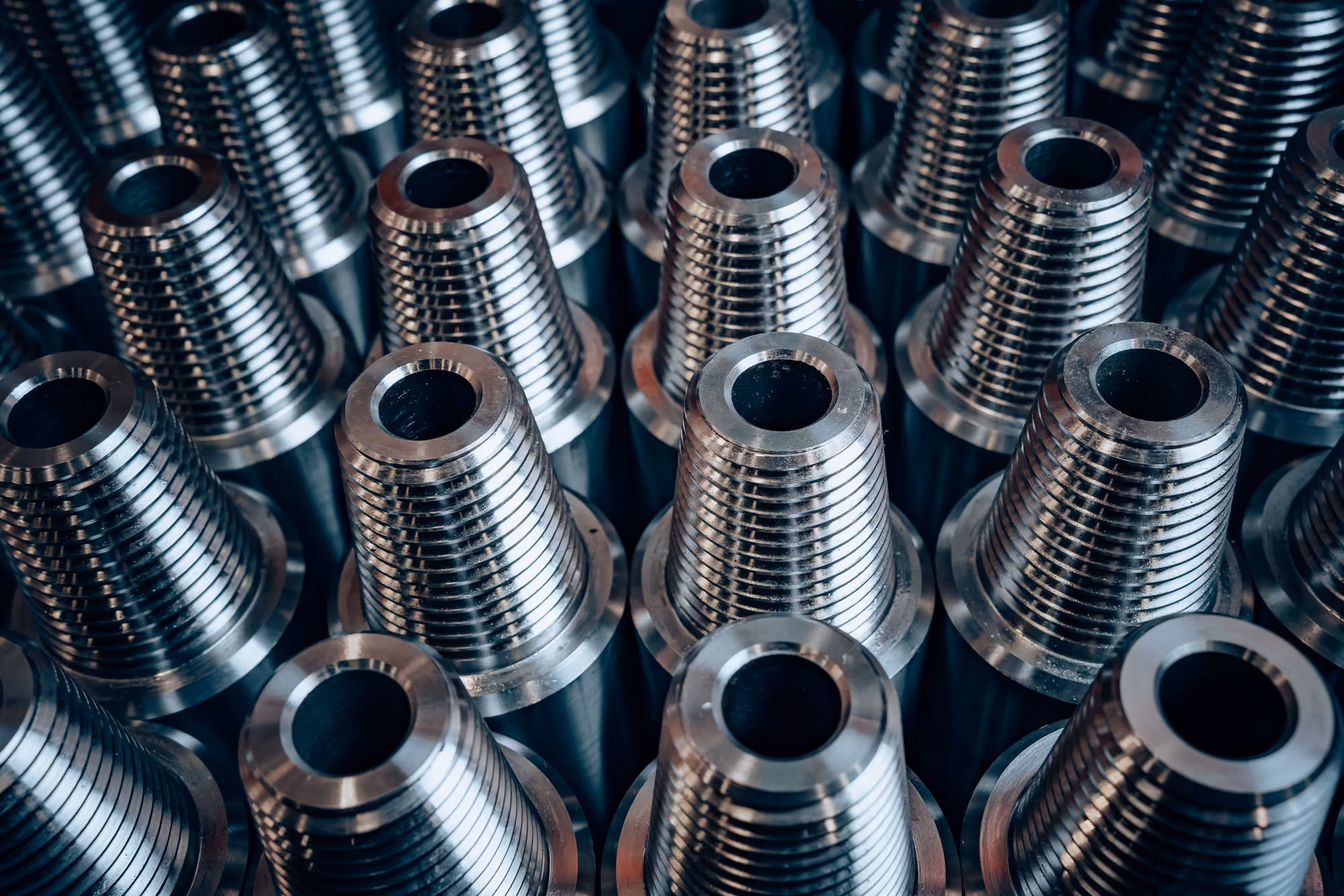 Close-up of multiple shiny metal threaded tool joints arranged in rows on a surface, used in industrial or mechanical applications.