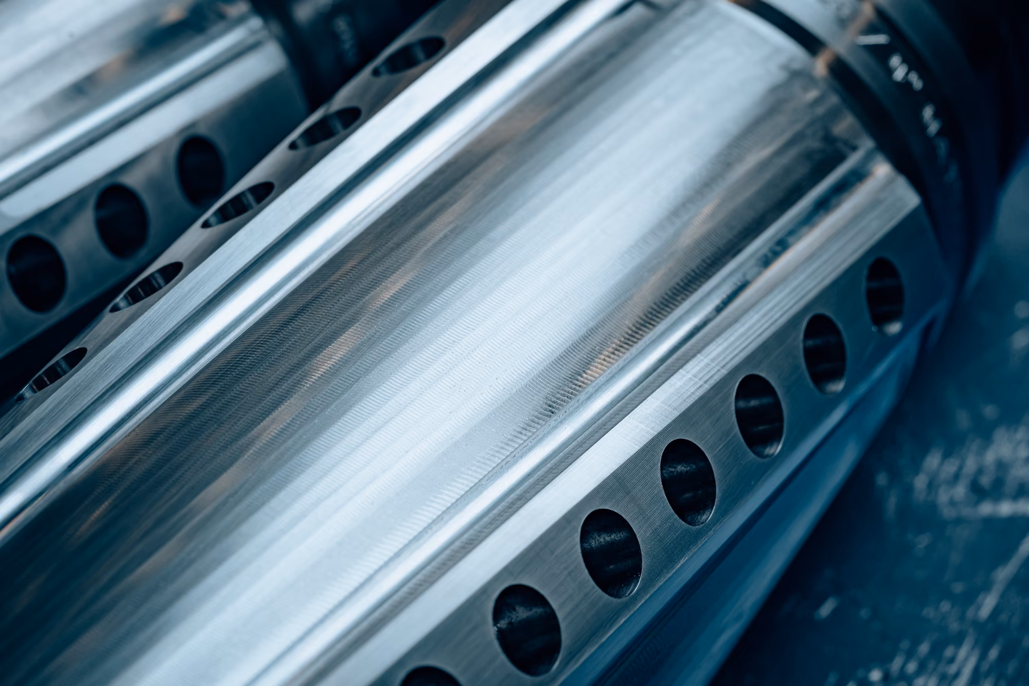 Close-up of shiny metallic cylindrical components with evenly spaced circular holes, showing polished and textured surfaces.