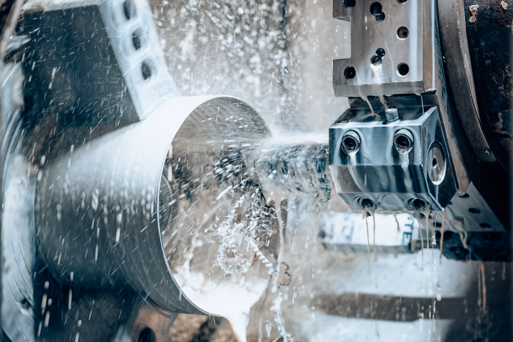 Close-up of a metalworking lathe machine shaping a cylindrical metal piece with coolant fluid spraying around.