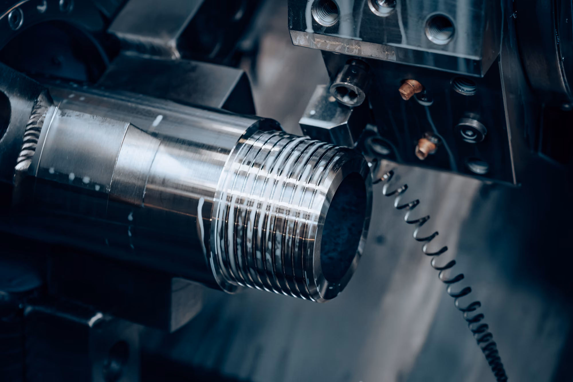 Close-up of a metal machining process showing a lathe cutting threads into a shiny cylindrical metal part.