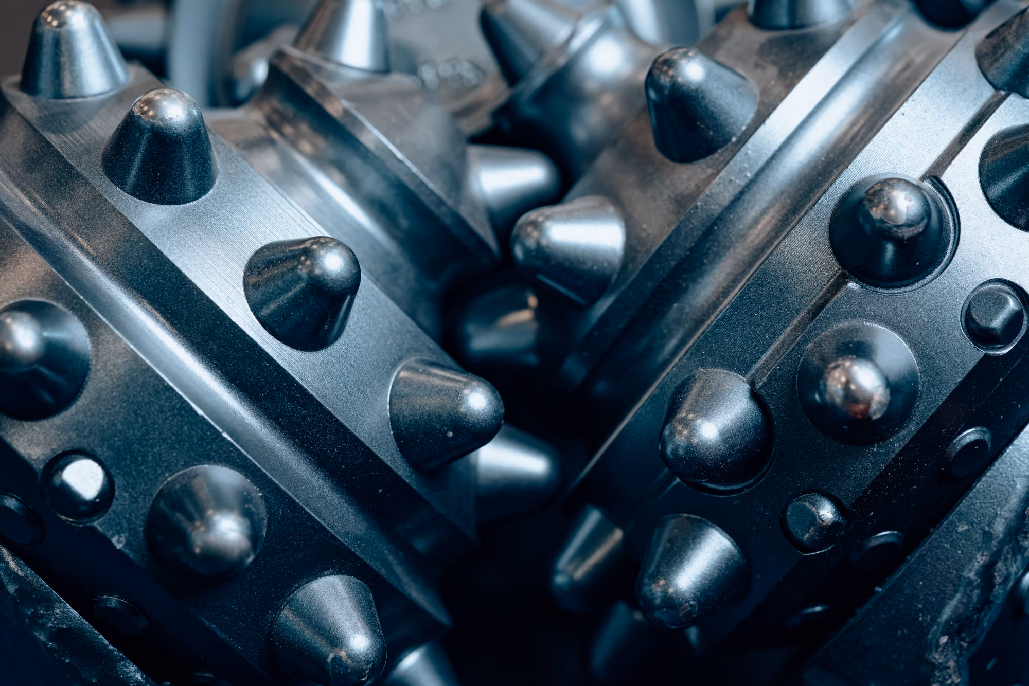 Close-up of metallic drill bits with conical protrusions used for industrial drilling or mining equipment.