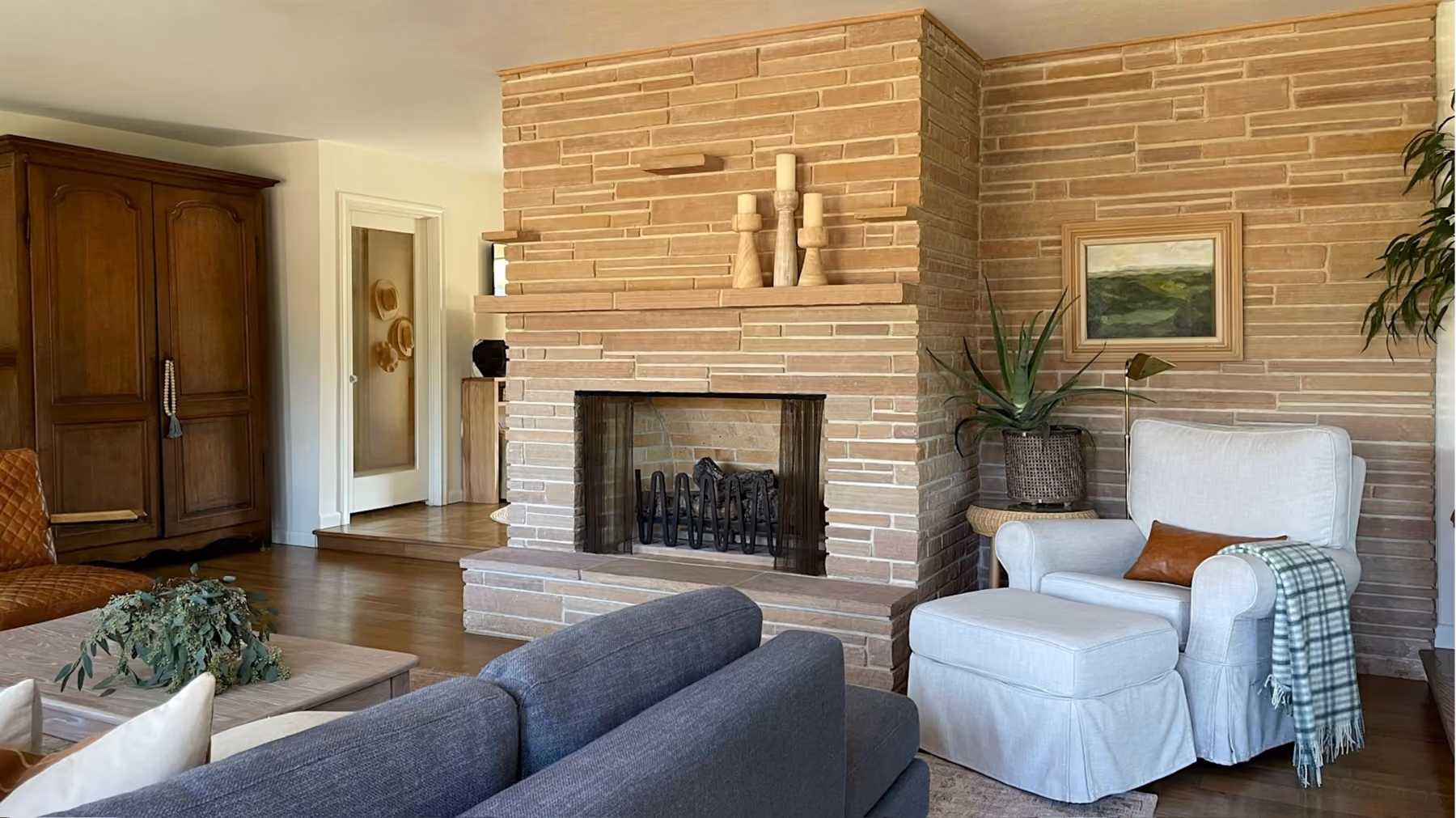 Cozy living room with stone fireplace, white armchair with ottoman, and gray sofa in front of wooden furniture.