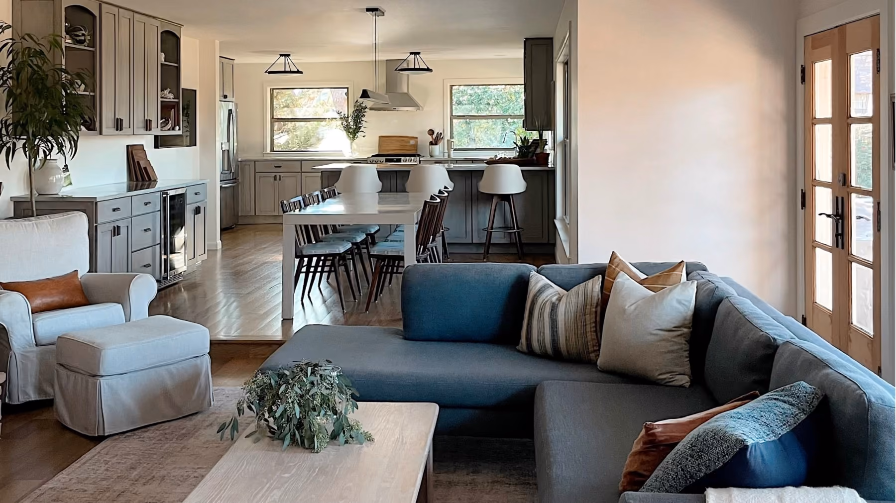 Open living room and kitchen with gray sectional sofa, armchair, dining table, and kitchen cabinets.