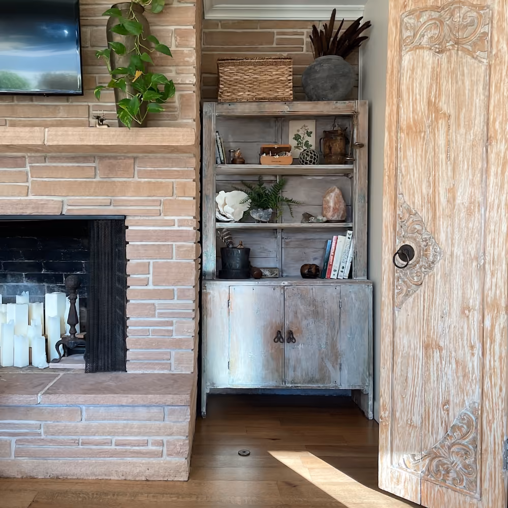 Cozy corner with a stone fireplace, wooden shelf filled with decor, and an ornate wooden door.