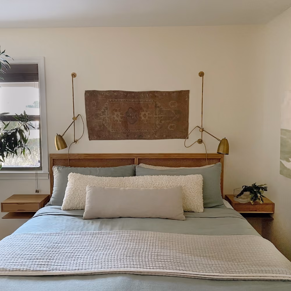 Cozy bedroom with blue bedding, textured pillows, wall tapestry, brass wall lamps, and floating nightstands.
