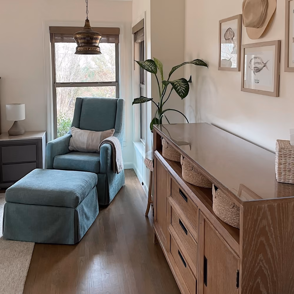 Cozy room with teal armchair, ottoman, wooden dresser with baskets, plant, and pendant light.