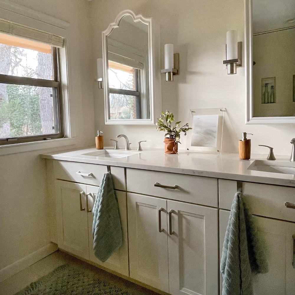 Modern bathroom with double sink vanity, wall mirrors, soft lighting, and small plant on countertop.