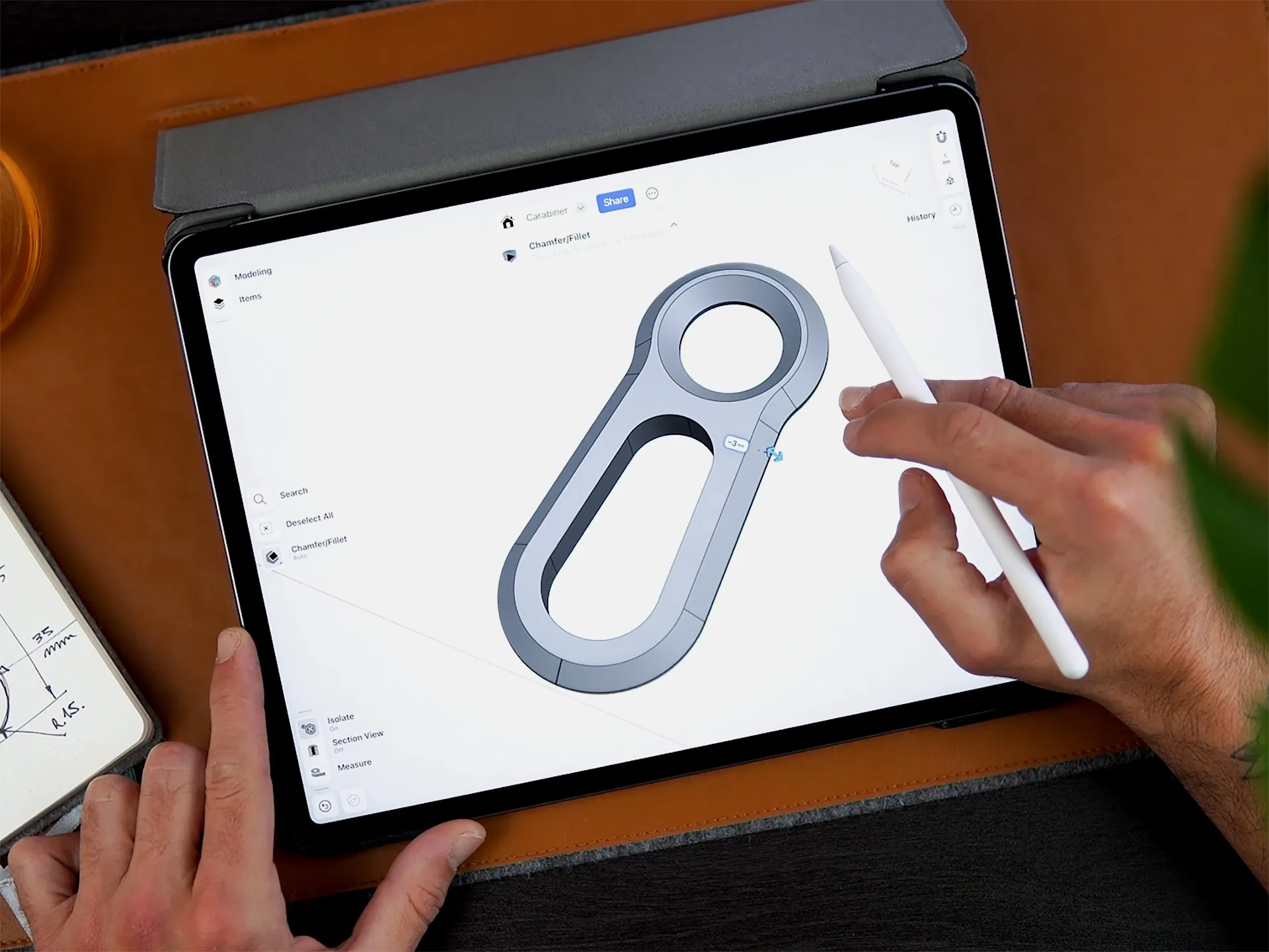 A hand using a stylus to design a 3D carabiner model on a tablet using Shapr3D.