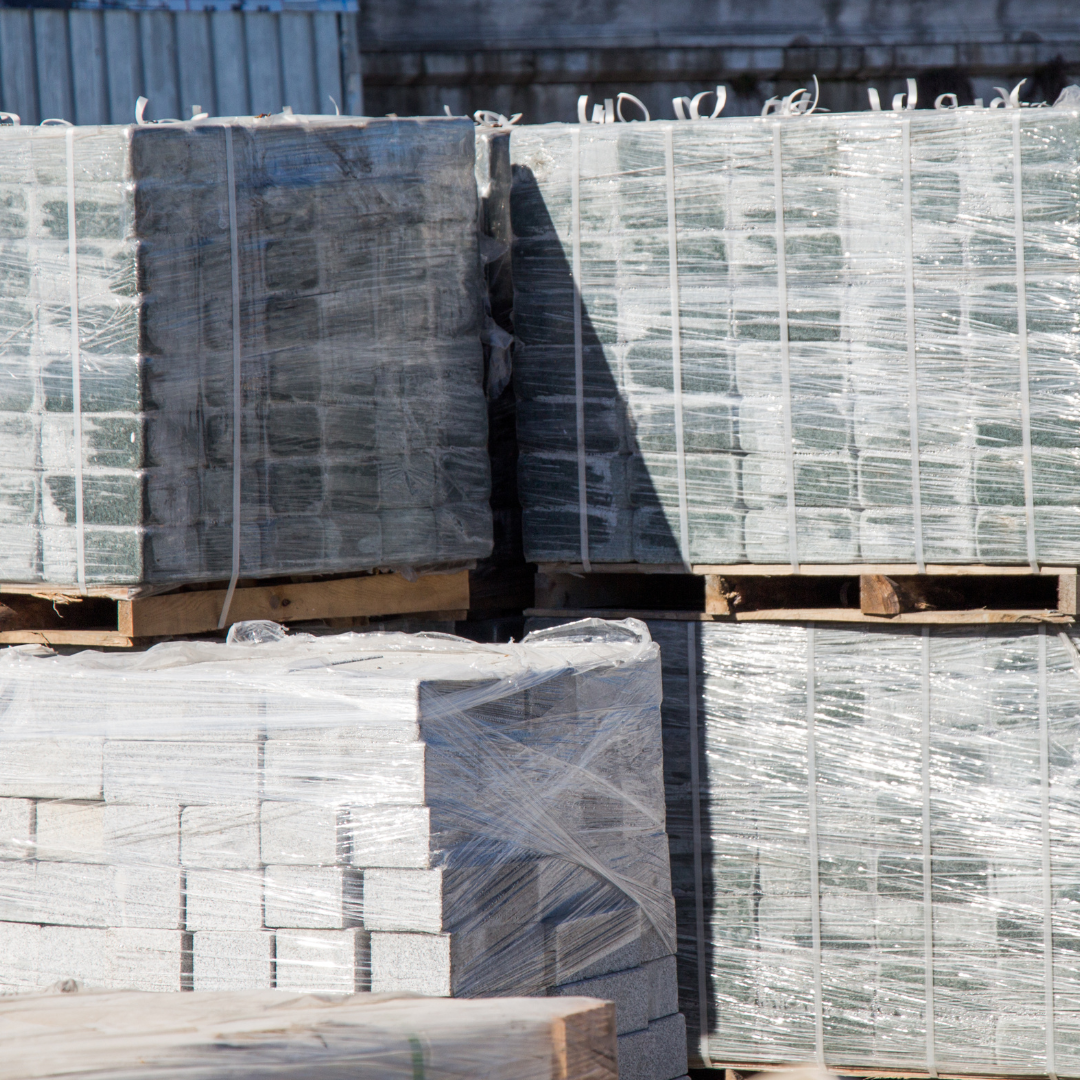 Stacks of bricks wrapped in plastic, placed on wooden pallets in an outdoor area.