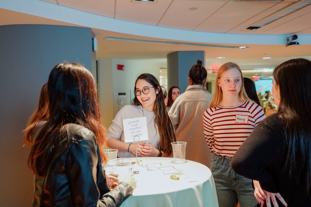 Five women standing around a small table and having a discussion.