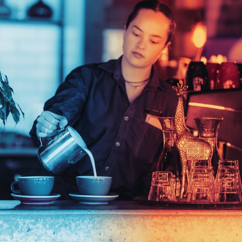 A barista pouring milk at the pass